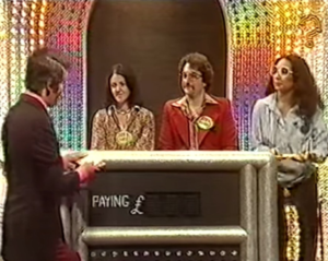 Host reading from a card to two contestants