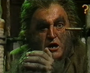 A hairy dirty man looks at an object next to the camera