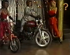 Two contestants on motorbikes in front of a lady
